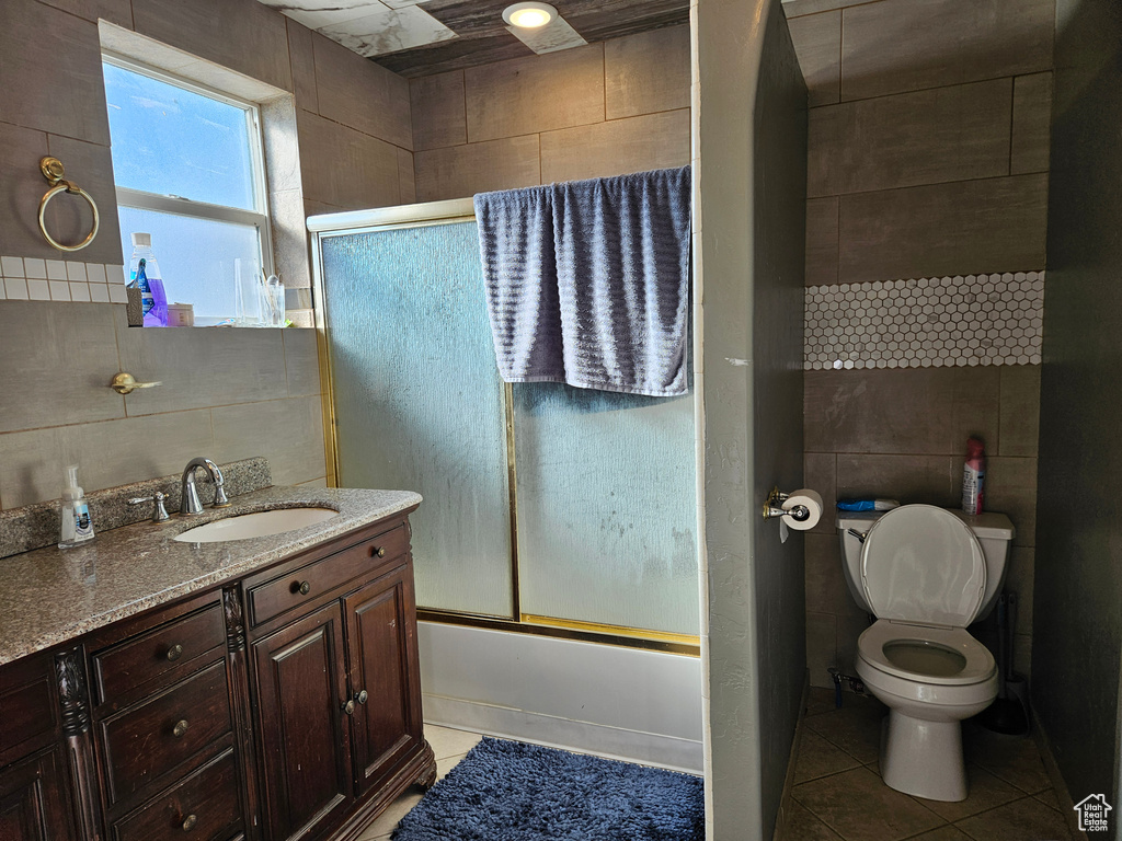 Bathroom with tile patterned flooring, tile walls, enclosed tub / shower combo, vanity, and toilet