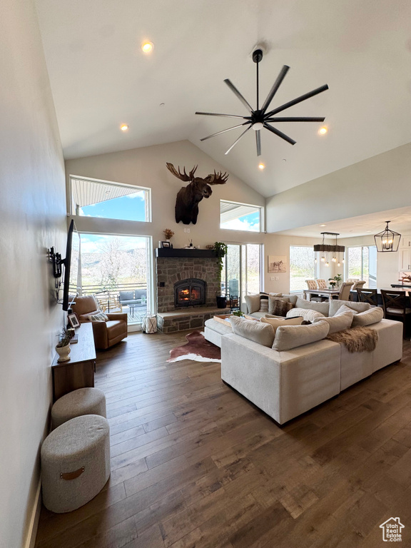 Living room featuring high vaulted ceiling, a lit fireplace, a ceiling fan, dark wood finished floors, and plenty of natural light