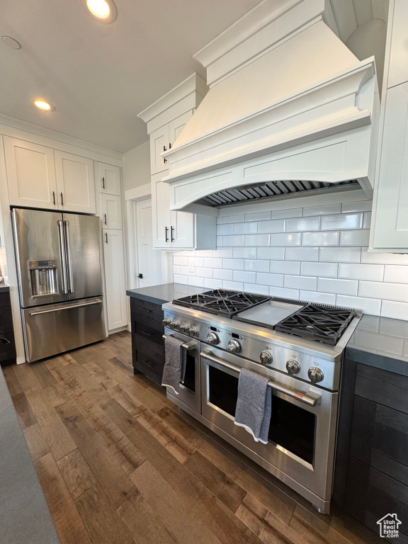 Kitchen with premium appliances, premium range hood, dark wood finished floors, white cabinets, and recessed lighting