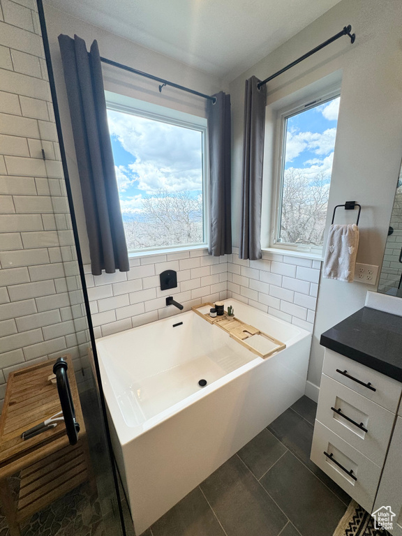 Full bathroom featuring plenty of natural light, tile patterned flooring, a bath, vanity, and tile walls