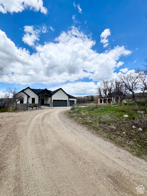 View of front of home featuring a garage, dirt driveway, and stone siding