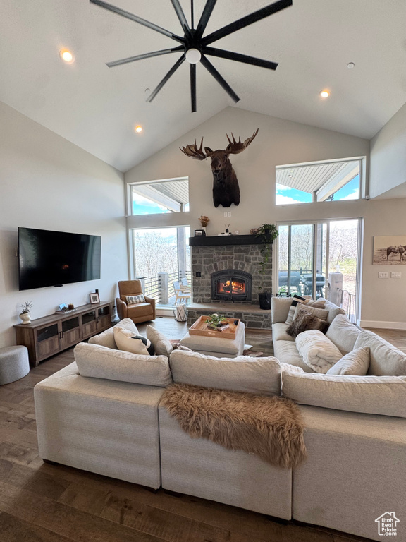Living room with high vaulted ceiling, a warm lit fireplace, wood finished floors, and recessed lighting