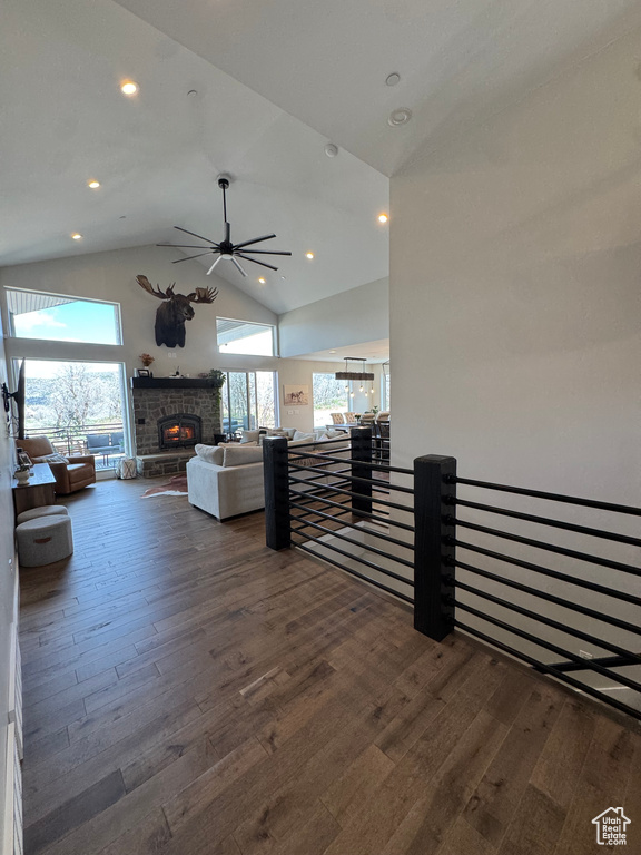 Living area featuring dark wood-style flooring, a ceiling fan, a stone fireplace, high vaulted ceiling, and recessed lighting