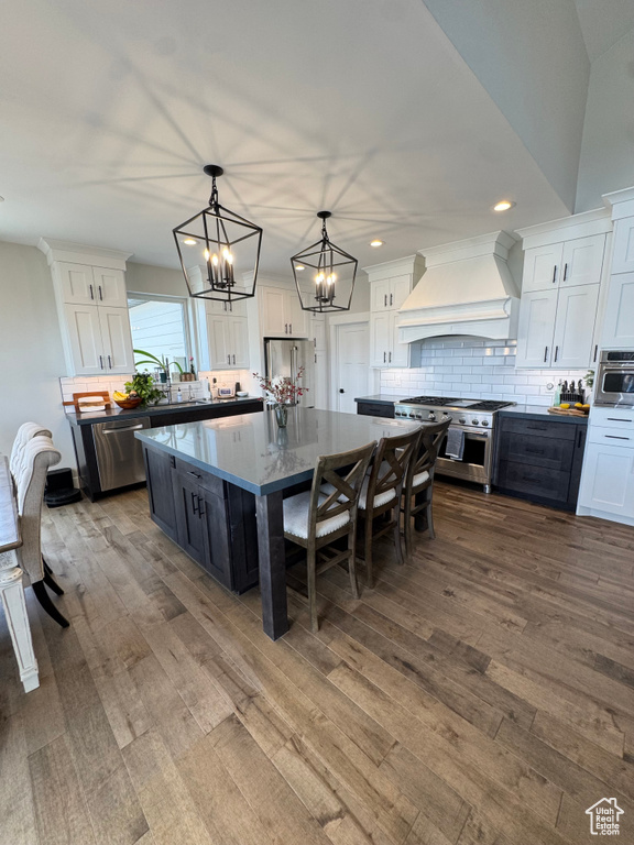 Kitchen with custom exhaust hood, stainless steel appliances, white cabinets, dark wood finished floors, and recessed lighting