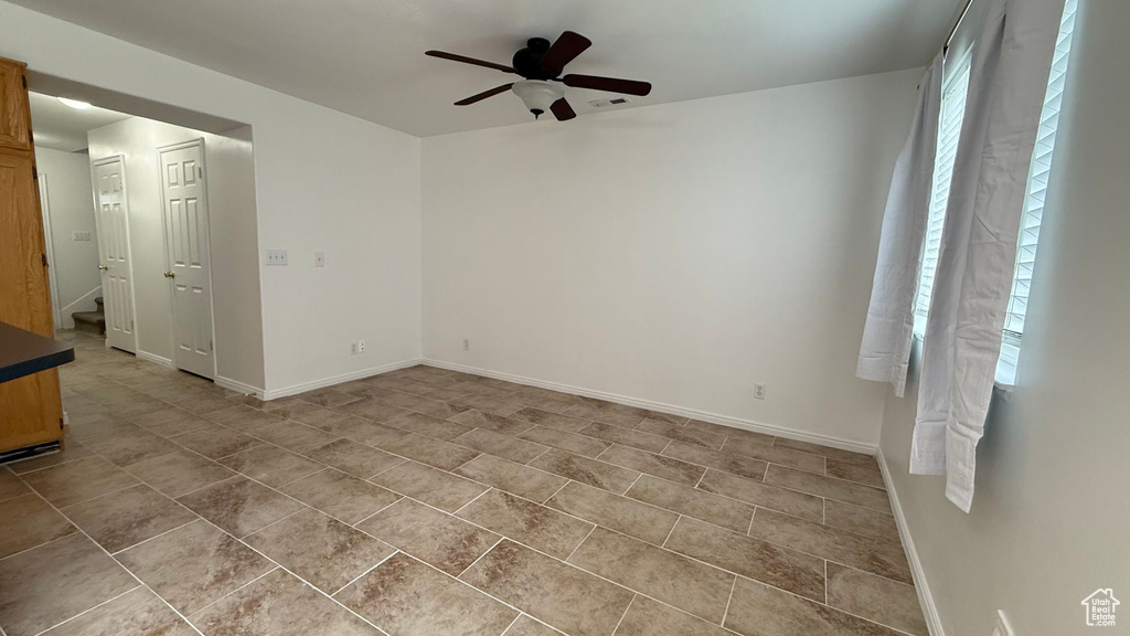 Unfurnished room featuring ceiling fan, baseboards, light tile patterned floors, and stairs