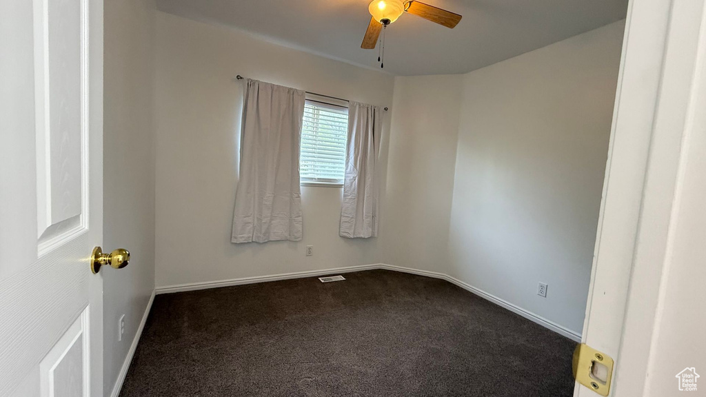 Empty room featuring dark colored carpet, ceiling fan, and baseboards