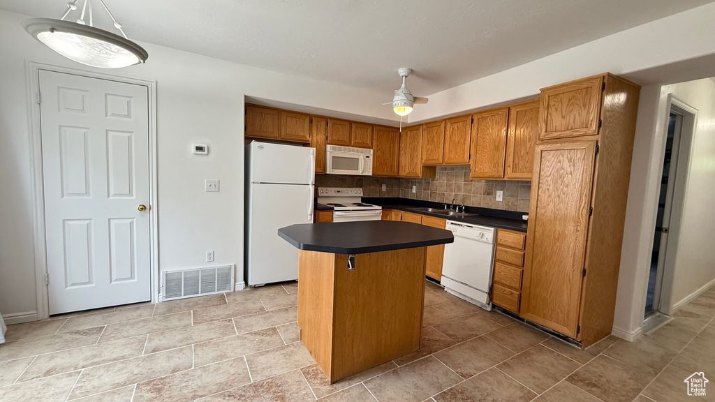 Kitchen featuring white appliances, dark countertops, a sink, backsplash, and a kitchen island