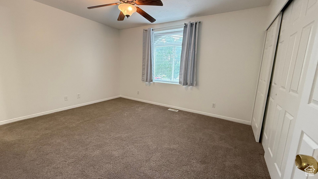 Unfurnished bedroom with dark carpet, a closet, baseboards, and ceiling fan
