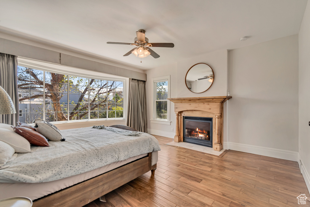 Bedroom featuring baseboards, a fireplace with flush hearth, wood finished floors, and ceiling fan