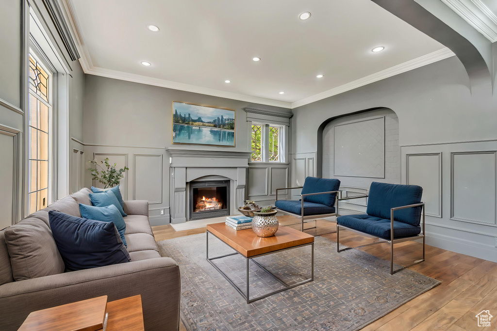 Living area featuring a decorative wall, wood finished floors, a warm lit fireplace, crown molding, and a wainscoted wall