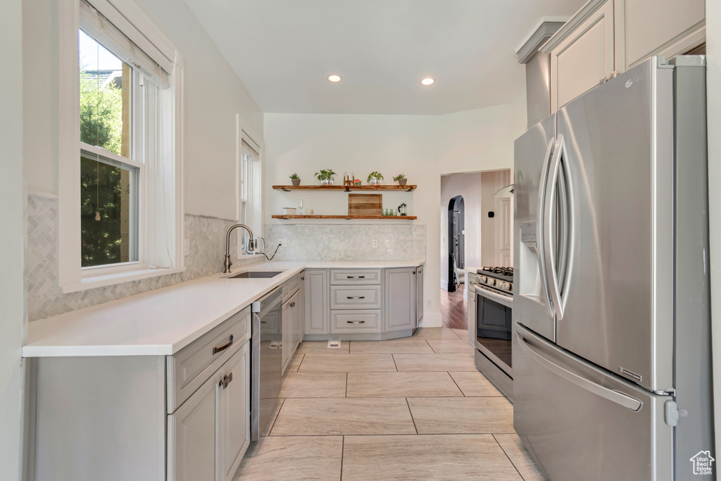 Kitchen featuring stainless steel appliances, open shelves, a sink, gray cabinets, and backsplash