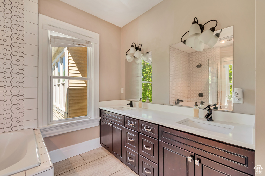 Bathroom featuring healthy amount of natural light, tiled shower, a tub, and double vanity