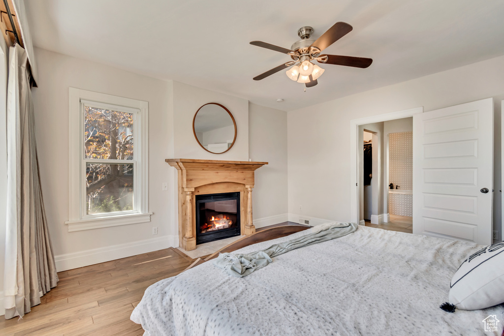 Bedroom featuring baseboards, a glass covered fireplace, light wood finished floors, and multiple windows