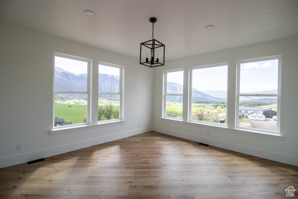 Unfurnished dining area featuring a chandelier, baseboards, a mountain view, and wood finished floors