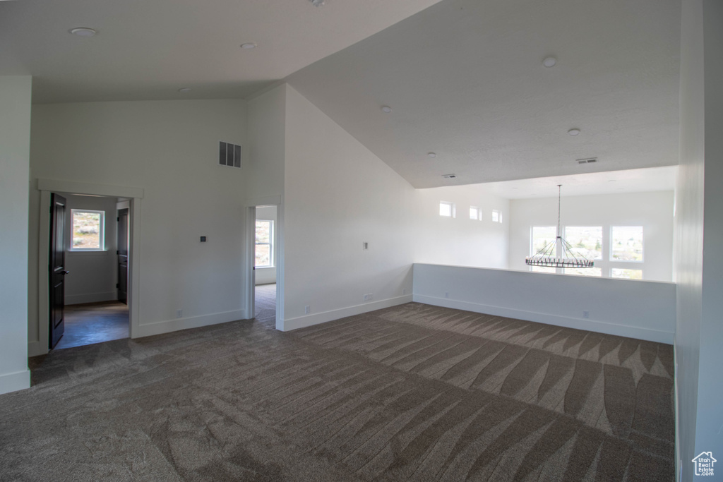 Carpeted empty room with a chandelier, baseboards, and high vaulted ceiling