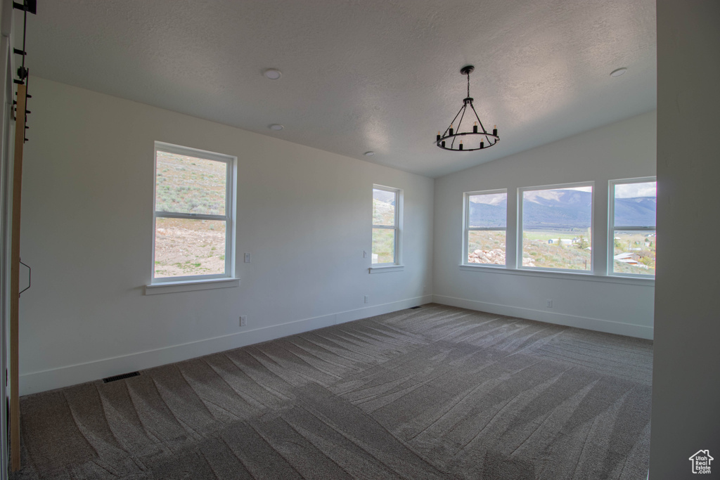 Carpeted empty room with baseboards, plenty of natural light, vaulted ceiling, and a textured ceiling