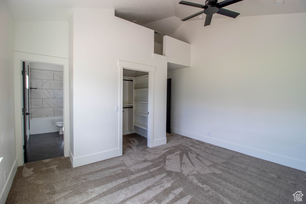 Unfurnished bedroom with carpet flooring, a walk in closet, high vaulted ceiling, baseboards, and ensuite bath