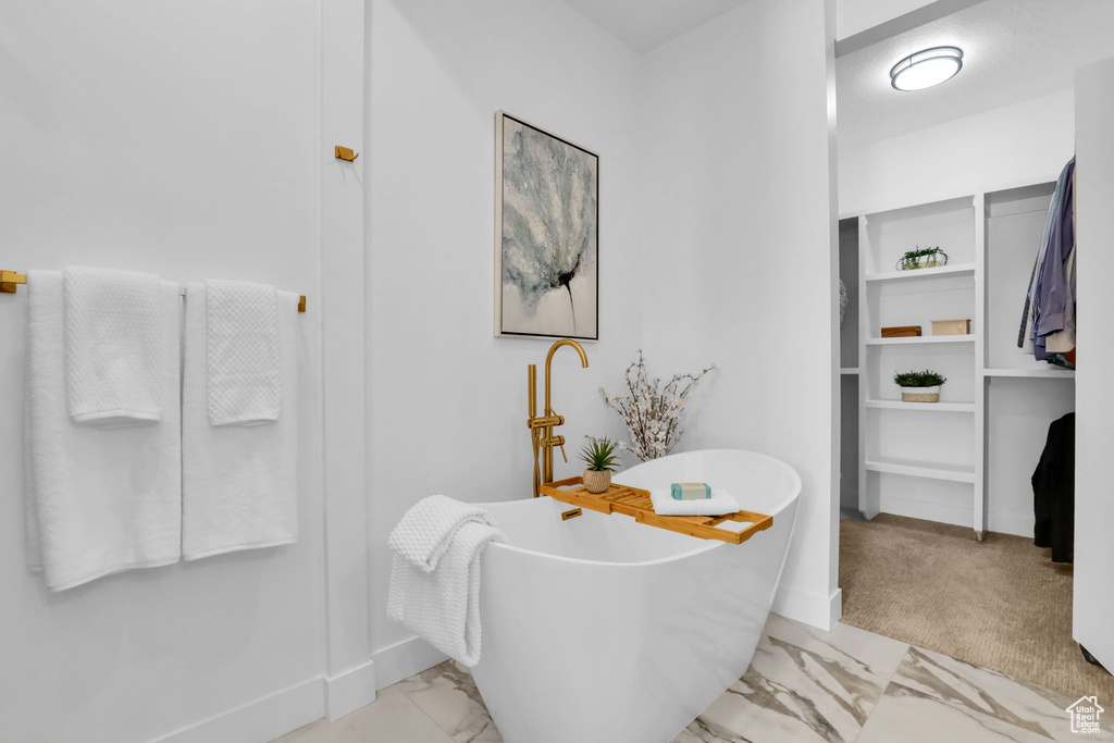 Bathroom featuring marble finish flooring, baseboards, and a freestanding tub