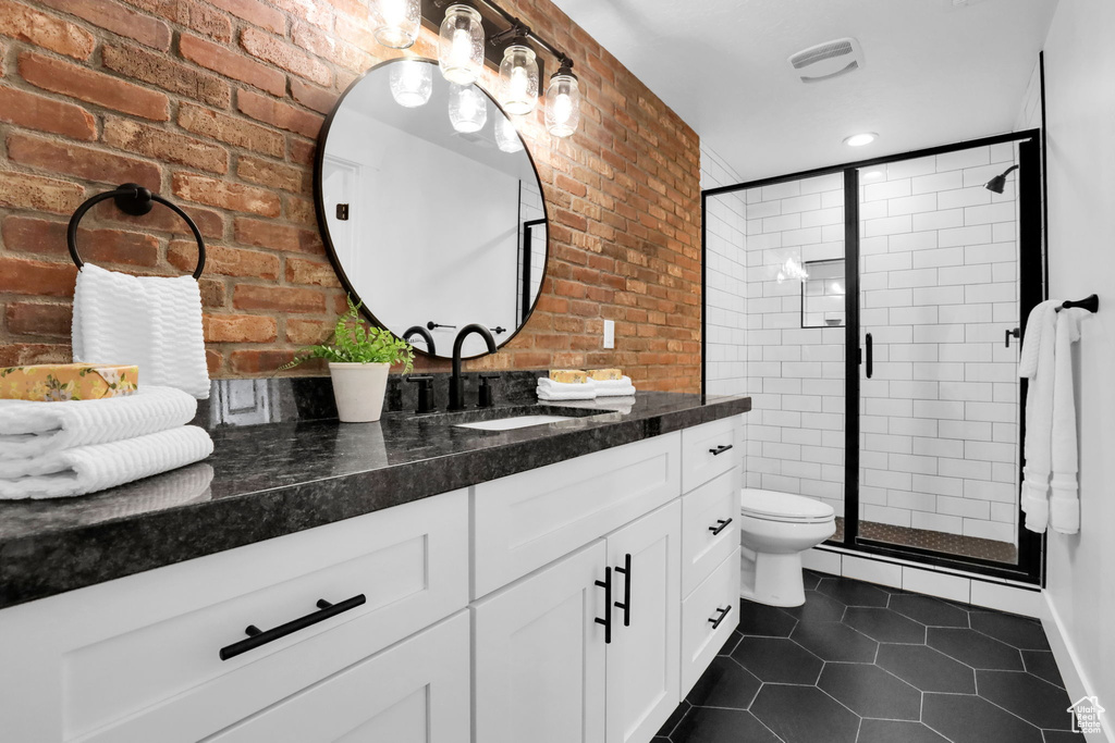 Bathroom featuring brick wall, tile patterned floors, a stall shower, vanity, and toilet