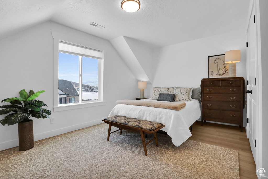 Bedroom featuring vaulted ceiling, light wood-type flooring, baseboards, and a textured ceiling