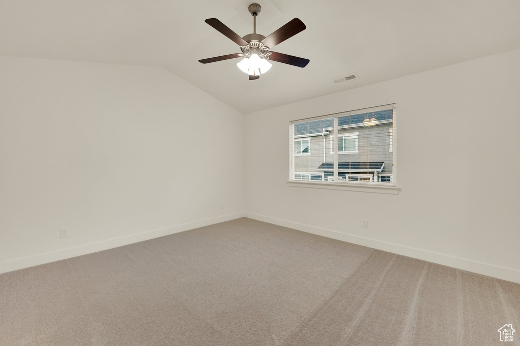 Empty room with vaulted ceiling, baseboards, light carpet, and ceiling fan