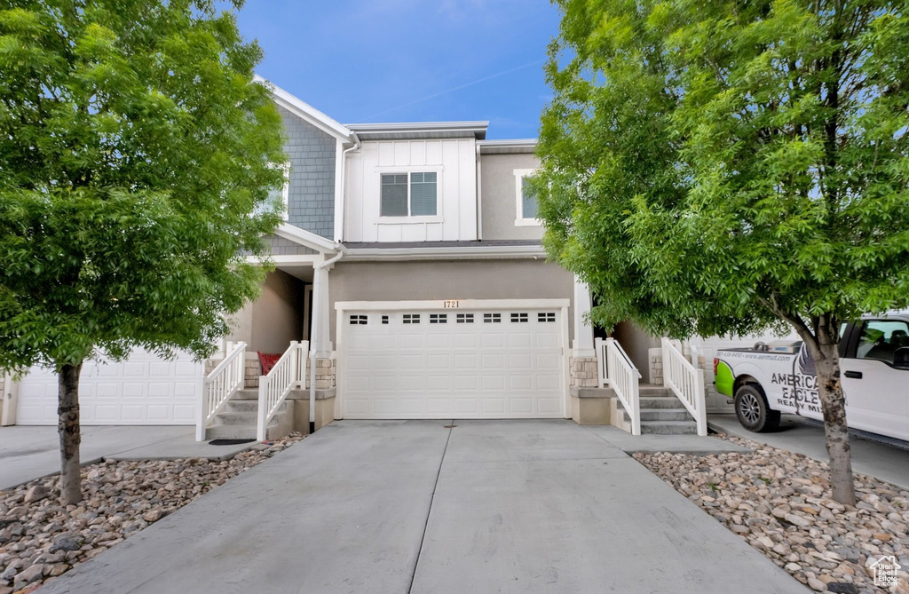 View of front of house featuring concrete driveway, stucco siding, a garage, stairs, and stone siding