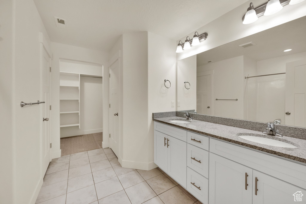 Bathroom featuring tile patterned flooring, double vanity, baseboards, a walk in closet, and a shower