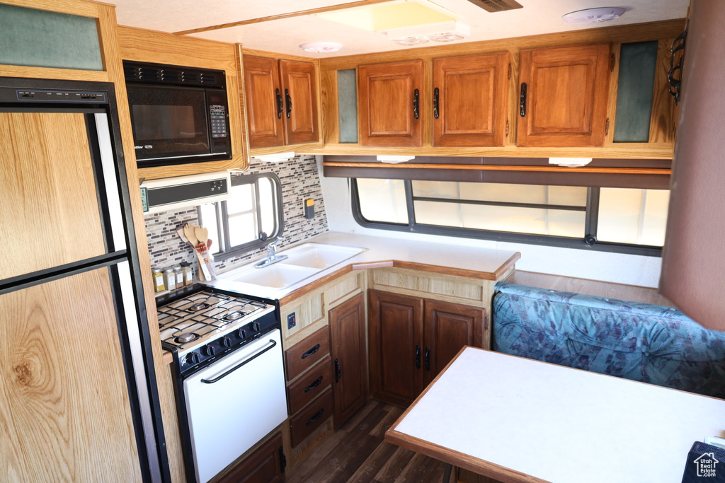 Kitchen with freestanding refrigerator, white gas stove, black microwave, light countertops, and dark wood-style flooring