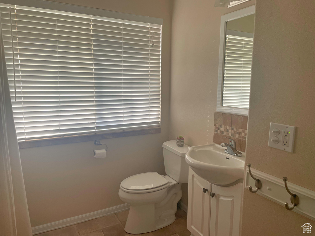 Half bath with toilet, vanity, tile patterned flooring, and backsplash