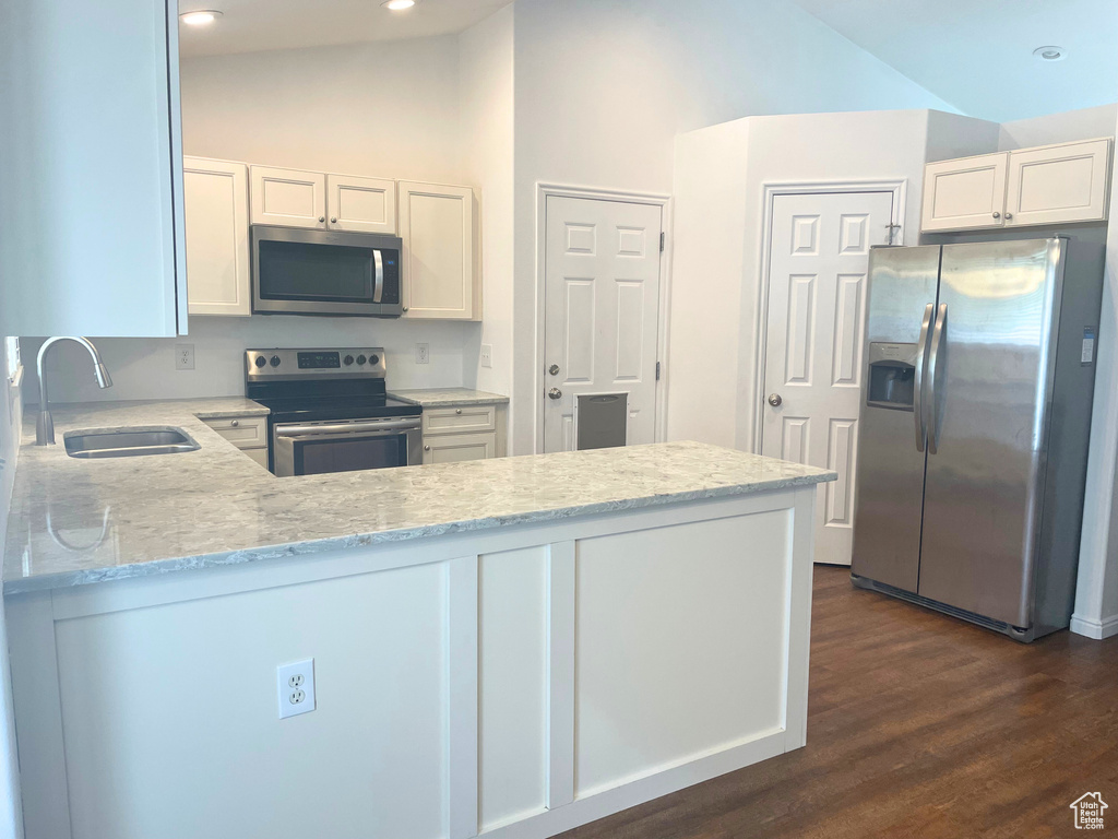Kitchen with appliances with stainless steel finishes, a sink, light stone countertops, a peninsula, and white cabinets