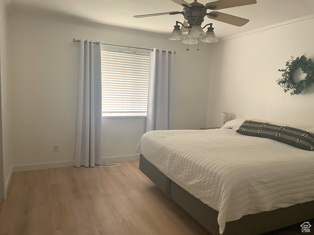 Bedroom featuring light wood-style floors, crown molding, a ceiling fan, and baseboards