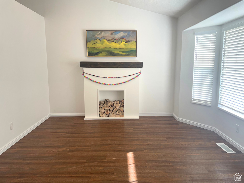Unfurnished room featuring wood finished floors, healthy amount of natural light, lofted ceiling, and baseboards