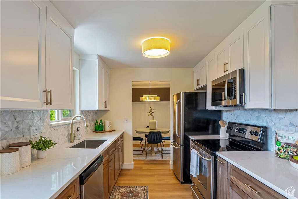 Kitchen featuring appliances with stainless steel finishes, a sink, light wood-type flooring, white cabinets, and decorative backsplash