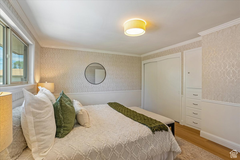 Bedroom with wood finished floors, a closet, ornamental molding, wallpapered walls, and baseboards