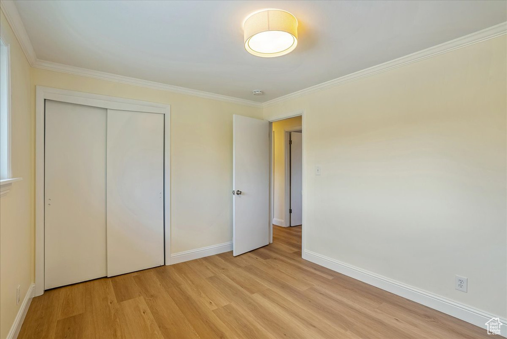 Unfurnished bedroom with light wood finished floors, baseboards, crown molding, and a closet