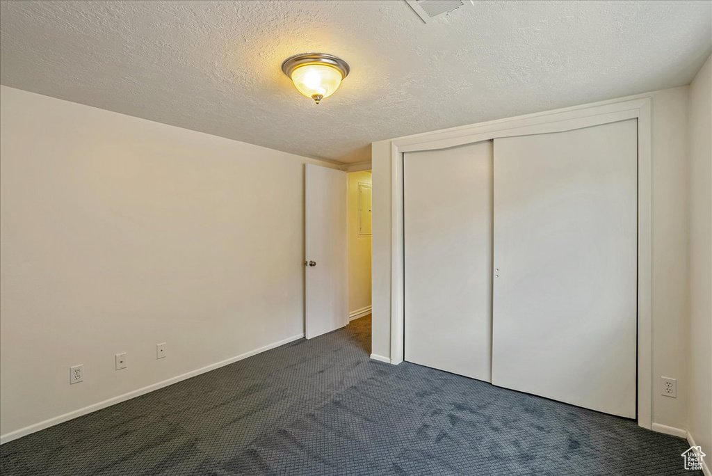 Unfurnished bedroom with dark carpet, a closet, a textured ceiling, and baseboards