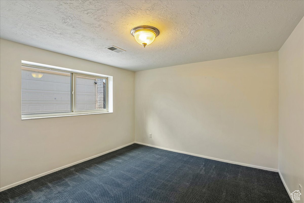 Empty room with dark colored carpet, baseboards, and a textured ceiling