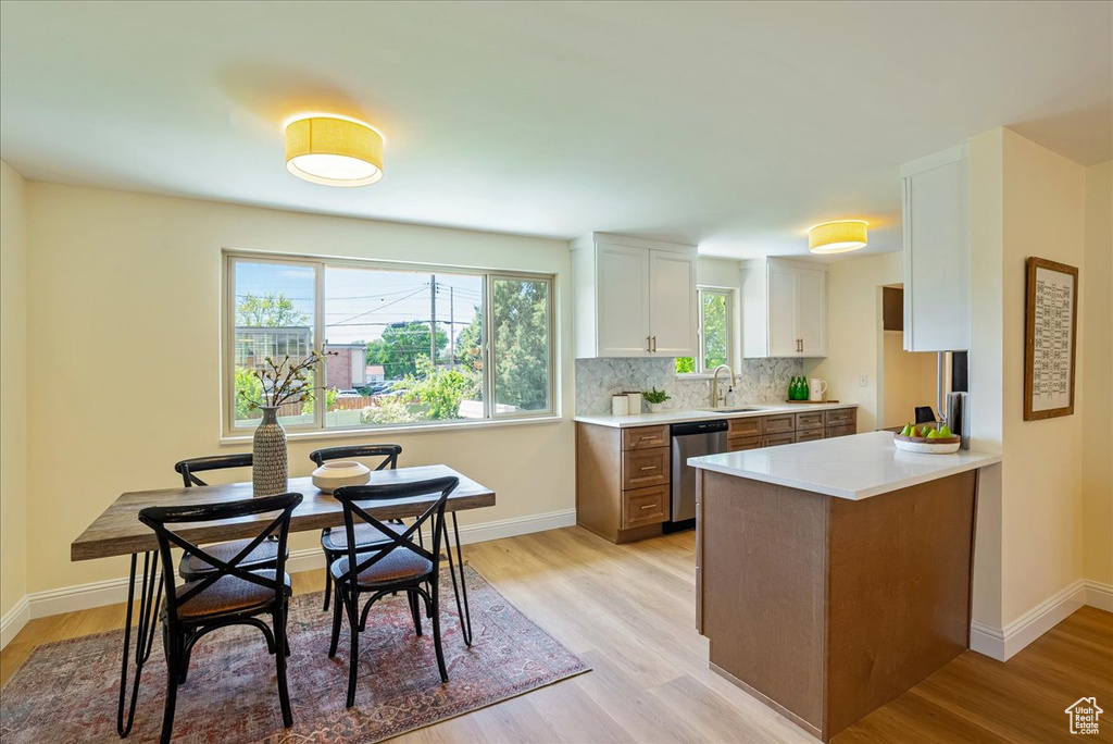 Kitchen with stainless steel dishwasher, light wood finished floors, white cabinets, light countertops, and baseboards