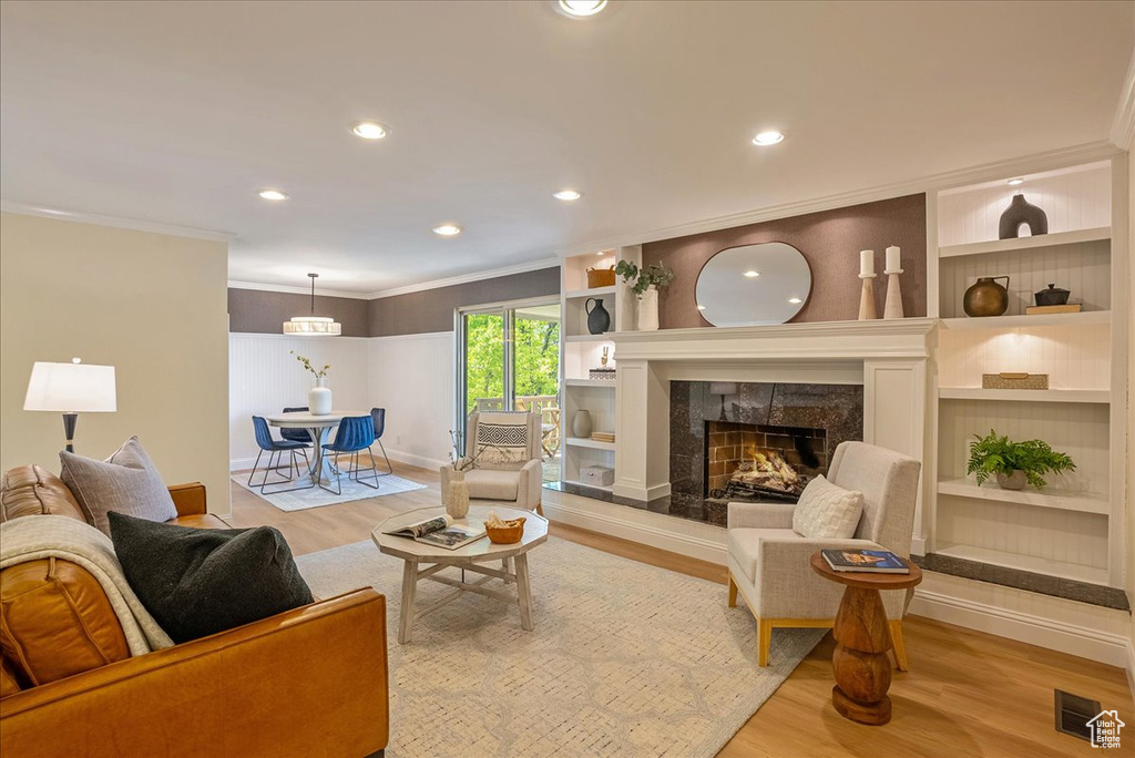 Living area featuring light wood finished floors, baseboards, a high end fireplace, crown molding, and built in features