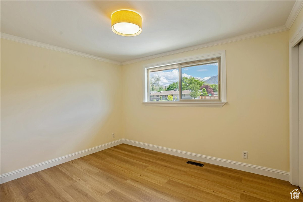Unfurnished room with light wood finished floors, baseboards, and crown molding