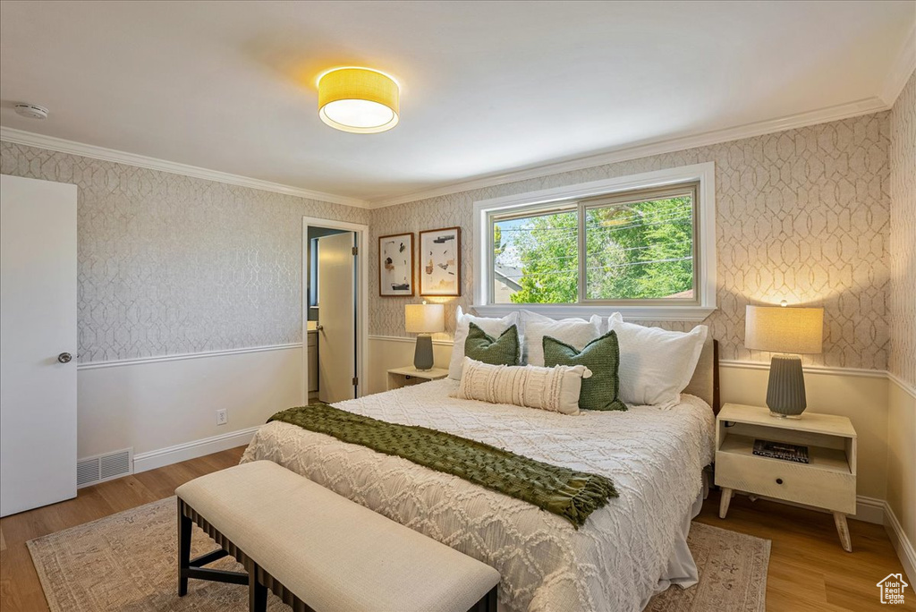 Bedroom featuring wood finished floors, crown molding, wallpapered walls, and baseboards