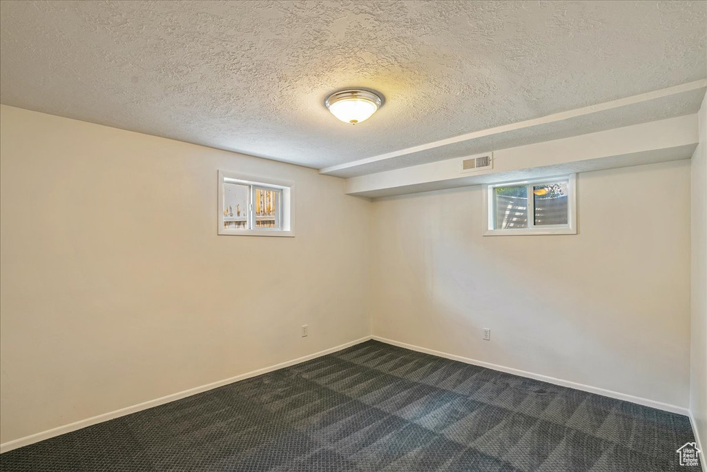 Basement with a textured ceiling, dark colored carpet, and baseboards