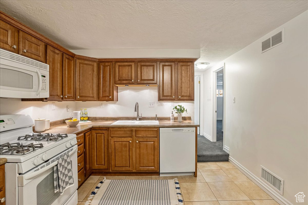 Kitchen featuring white appliances, a sink, brown cabinetry, and a textured ceiling