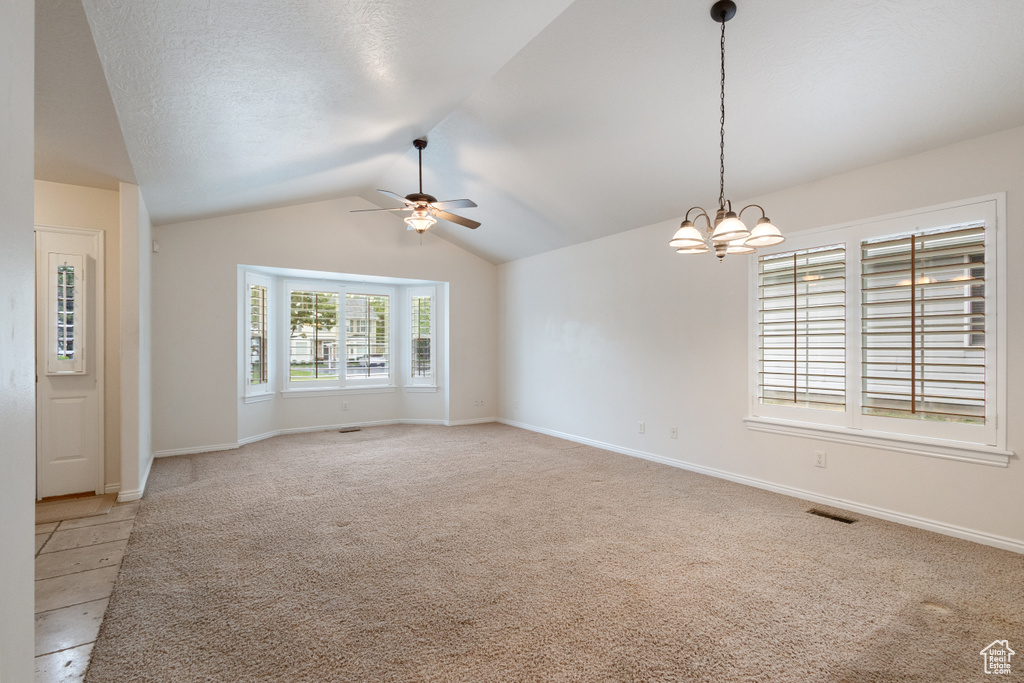 Unfurnished room featuring a ceiling fan, vaulted ceiling, light carpet, a chandelier, and baseboards