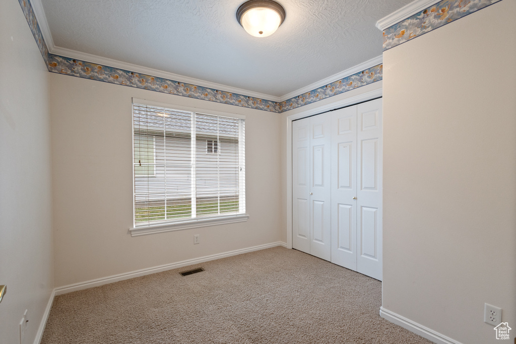 Unfurnished bedroom featuring a closet, carpet floors, baseboards, a textured ceiling, and crown molding