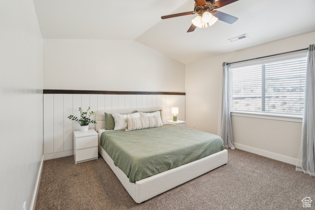 Bedroom featuring vaulted ceiling, carpet flooring, a wainscoted wall, and a ceiling fan