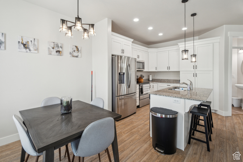 Kitchen featuring appliances with stainless steel finishes, a sink, light wood-type flooring, white cabinets, and a kitchen island with sink