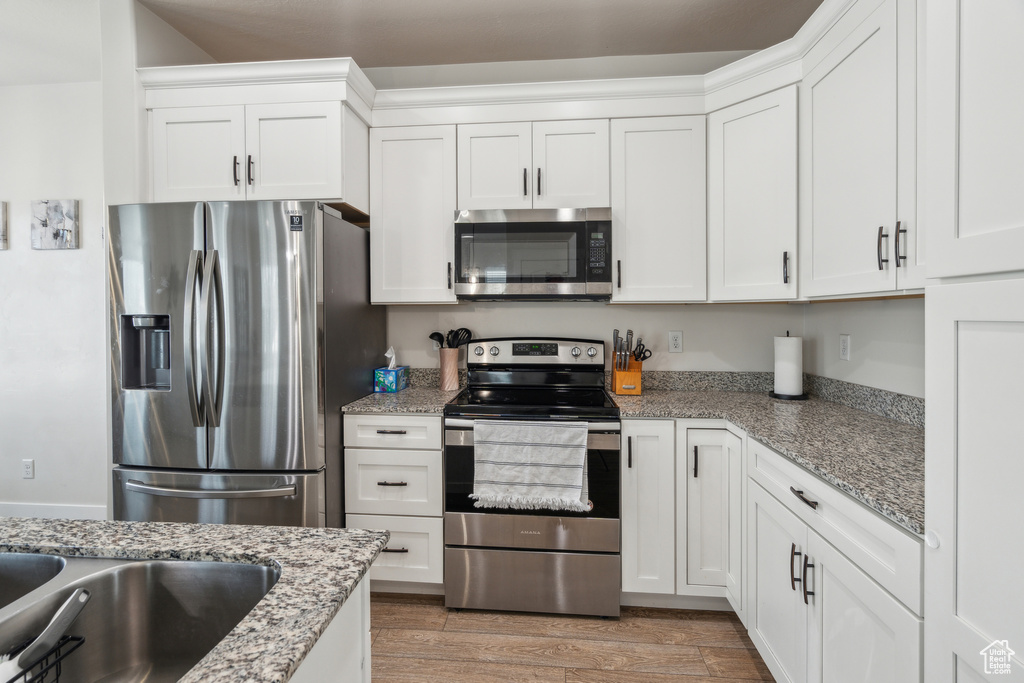 Kitchen with stainless steel appliances, white cabinetry, light wood-style flooring, and light stone countertops