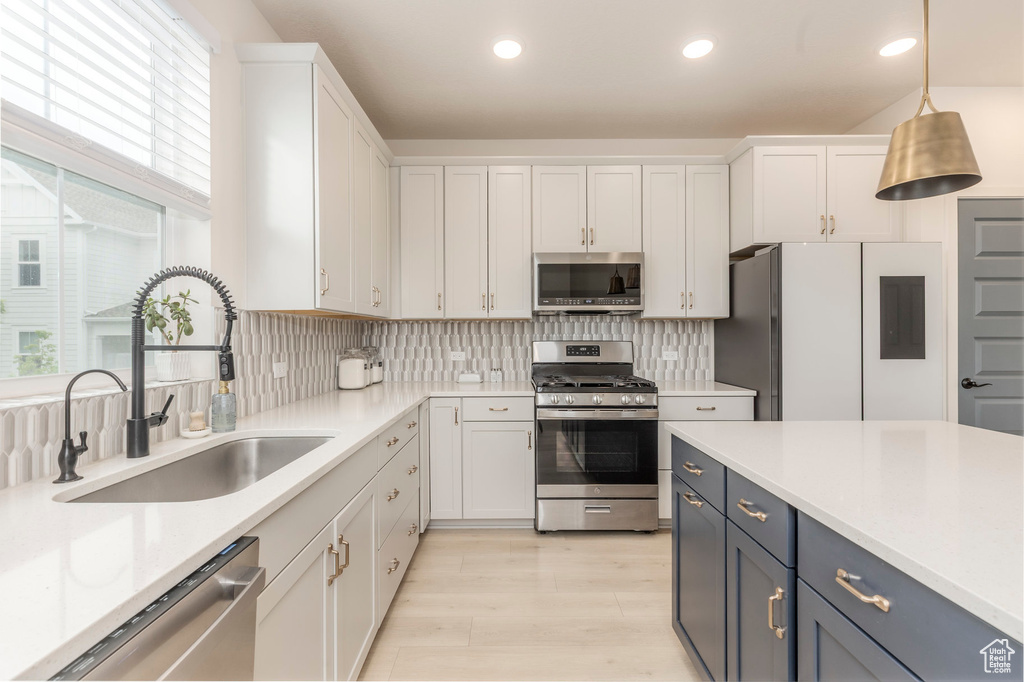 Kitchen featuring appliances with stainless steel finishes, a sink, light countertops, white cabinets, and hanging light fixtures