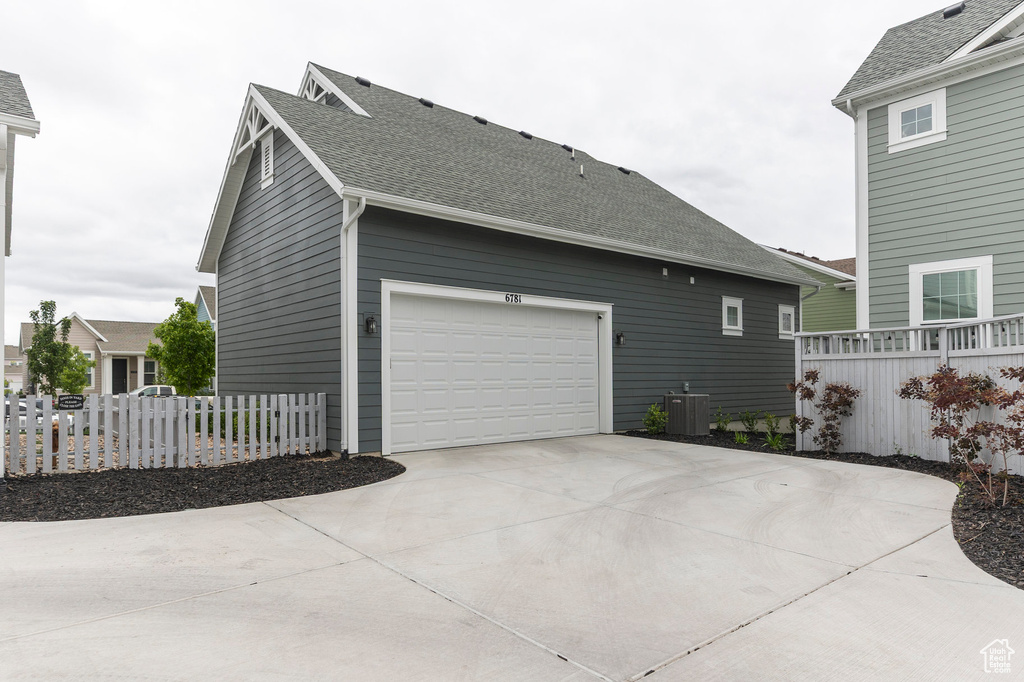 View of property exterior featuring central AC unit, fence, a garage, concrete driveway, and a shingled roof